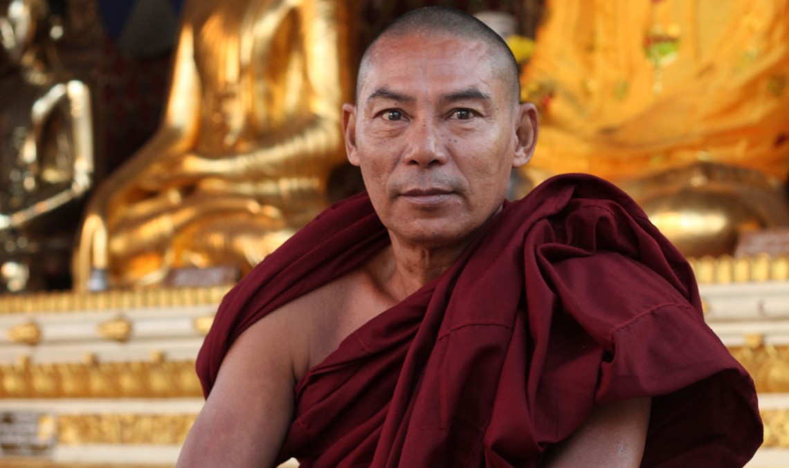 The Global Girl Travels: Powerful monk in deep oxblood robes sitting at the steps of one of the golden Buddha temples at Shwedagon Pagoda in Yangon, Myanmar.