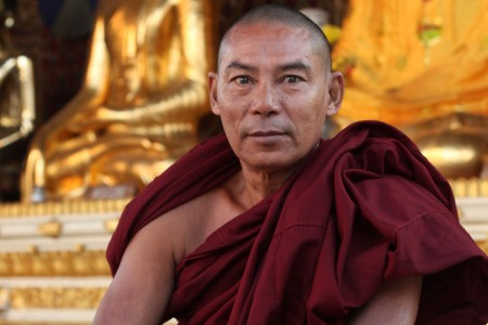 The Global Girl Travels: Powerful monk in deep oxblood robes sitting at the steps of one of the golden Buddha temples at Shwedagon Pagoda in Yangon, Myanmar.